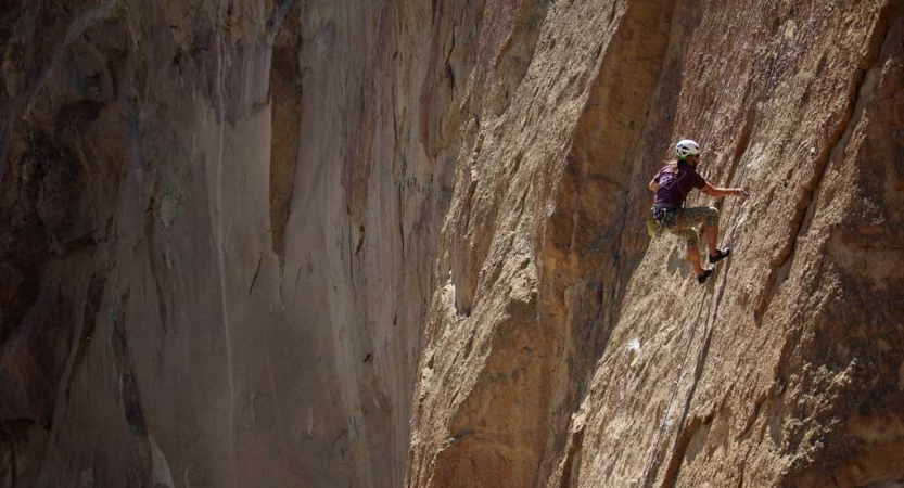 Wearing safety gear and secured by ropes, a person climbs a steep rock wall.